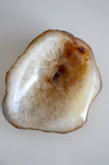 A cream and orange agate bowl sits on a white table in front of an orchid plant