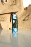 A Labradorite Tower crystal with an intense blue flash stands on a white table. In the background are 23 Urban branded jute bags. 