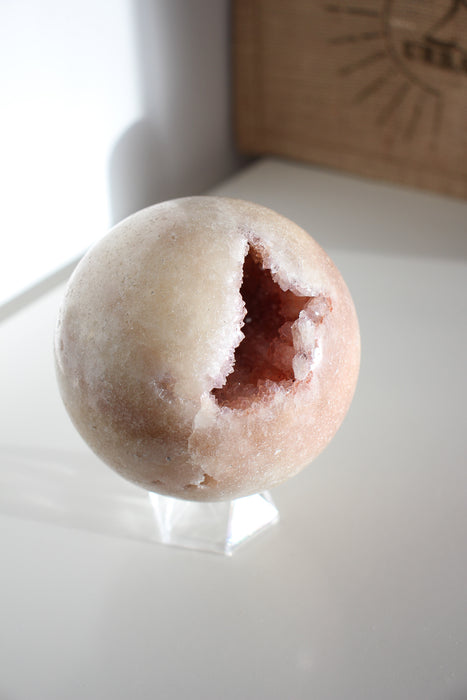 A Pink Amethyst Sphere with druzy caves in front of a green plant