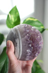 A large juicy purple Amethyst Sphere is held up by a hand in the afternoon sunlight