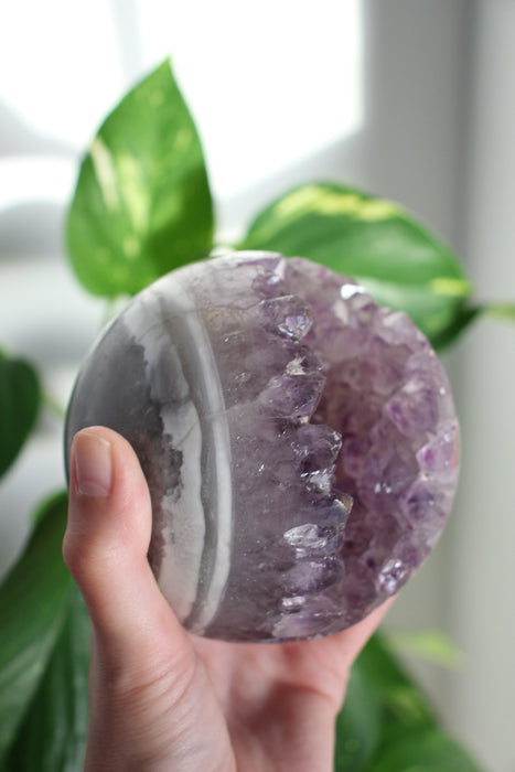 A large juicy purple Amethyst Sphere is held up by a hand in the afternoon sunlight