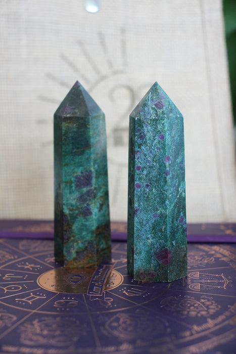 Two Ruby in Kyanite towers stand on a purple surface in front of a 23 Urban branded jute bag