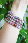 Beautiful pink tourmaline bracelets stacked on a wrist in front of a green plant 