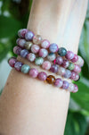 Beautiful pink tourmaline bracelets stacked on a wrist in front of a green plant 