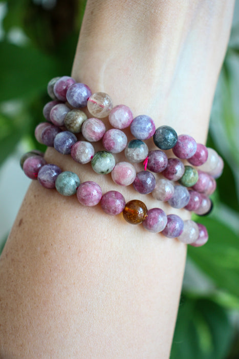 Beautiful pink tourmaline bracelets stacked on a wrist in front of a green plant 