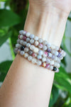 A stack of beautiful small bead pale Pink Tourmaline bracelets on a wrist in front of a green plant.