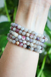 A stack of beautiful small bead pale Pink Tourmaline bracelets on a wrist in front of a green plant.