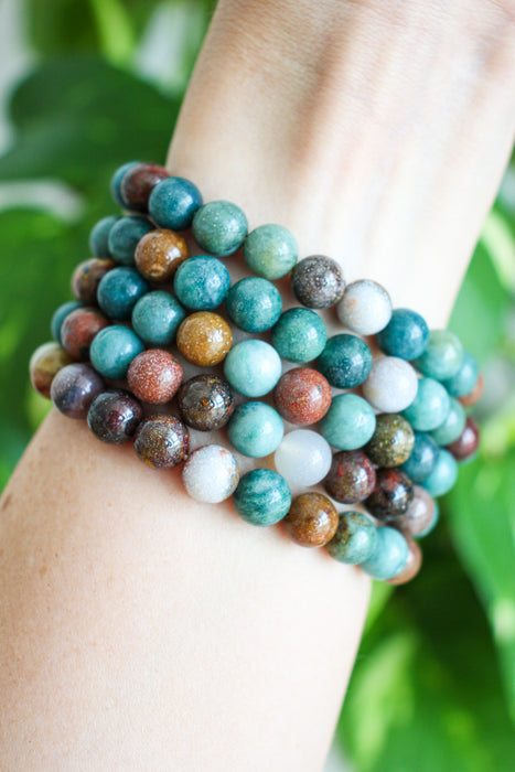 Beautiful blue and brown toned Ocean Jasper, pictured stacked on a wrist in front of a green plant