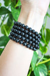 Matte black Shungite Bracelets stacked on a wrist in front of a green plant 