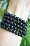 Matte black Shungite Bracelets stacked on a wrist in front of a green plant 