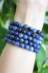 A deep blue stack of Sodalite bracelets in front of a green plant 