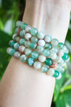 A stack of Green Flower Agate bracelets on a wrist in front of a green plant 