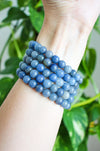 A stack of Blue Aventurine bracelets in a bright sky blue colour, on a wrist in front of a green plant. 