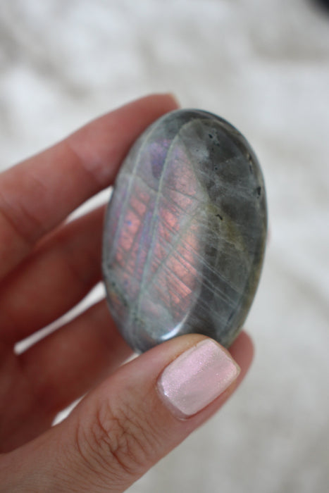 Pink and Purple flash Labradorite Palm Stone in front of a green background. 23 Urban. Dubai crystals.