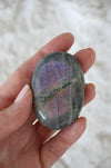 Pink and Purple flash Labradorite Palm Stone in front of a green background. 23 Urban. Dubai crystals.