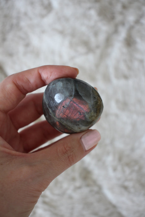 Pink flash Labradorite Palm Stone in front of a cream background. 23 Urban. Dubai crystals.